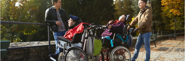 Foto von zwei Menschen im Rollstuhl und ihren Assistenten in der Natur