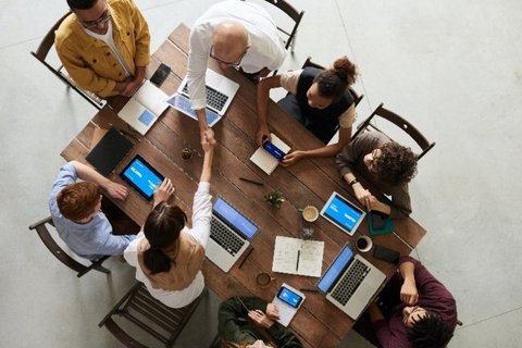Menschen sitzen rund um einen Tisch und arbeiten mit Laptops