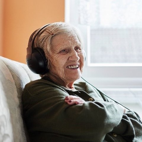 Ältere Frau mit Kopfhörern sitzt in einem Sessel